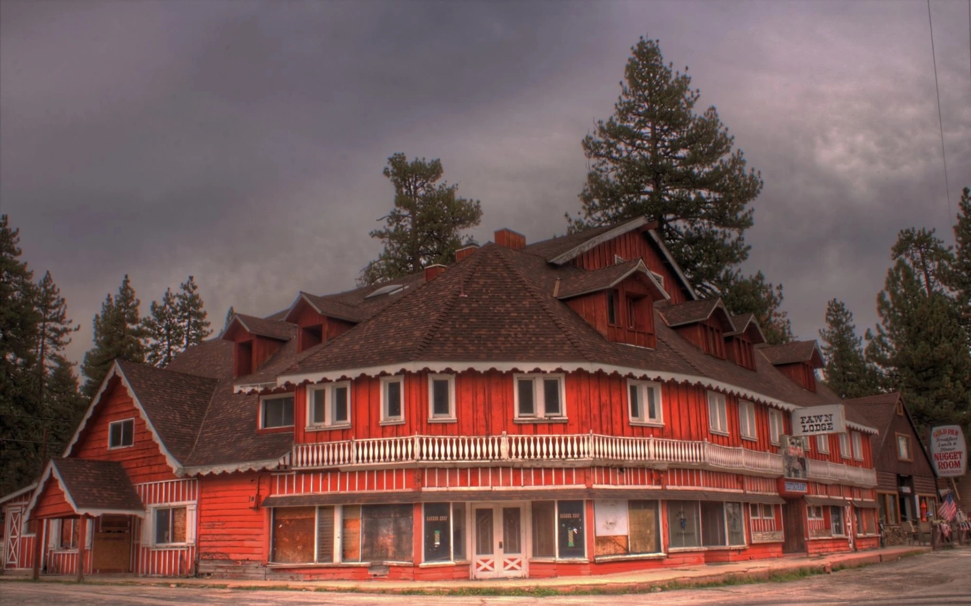 The Fawn Lodge exterior today, a weathered red wooden building with boarded windows and the Fawn Lodge sign, under an overcast sky in Fawnskin.
